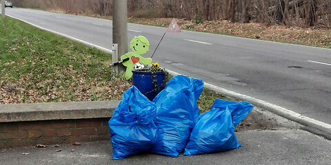 3 blauen Müllsäcke neben vor einem grünen Aufsteller, der ein Kind darstellt.