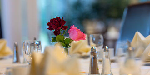 Ein stilvoll gedeckter Tisch im Restaurant Rosenflair. In der Mitte des Tisches stehen zwei Rosen in Rosa und Dunkelrot als dekorativer Blickfang.