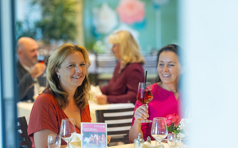 Die Teilnehmer der Romantischen Nachtführung genießen das Abendessen an stilvoll gedeckten Tischen im Restaurant Rosenflair. Im Hintergrund sind große Rosenmotive an der Wand zu sehen.