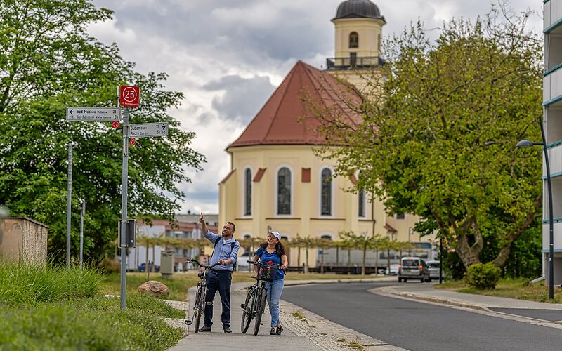 Zwei Radfahrende stehen am Knotenpunkt 25. Im Hintergrund ist die Stadtkirche St. Nikolai zu sehen.