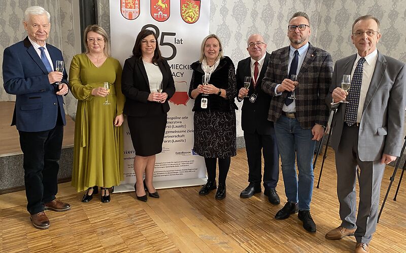 Die Vertreter der Städte stehen mit Sektgläsern vor einem Banner mit den Wappen der 3 Städten.