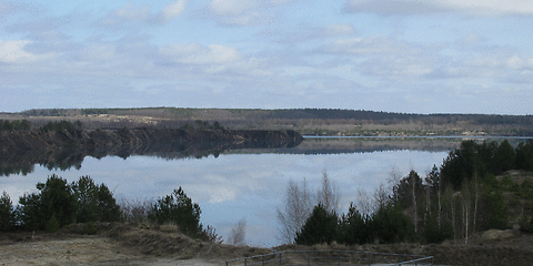 der Klinger See bei Sonnenschein – die Wolken spiegeln sich im Wasser, vorn ist das Einlaufbauwerk zu sehen
