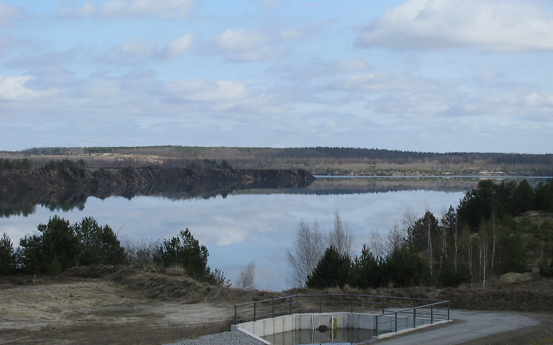 der Klinger See bei Sonnenschein – die Wolken spiegeln sich im Wasser, vorn ist das Einlaufbauwerk zu sehen