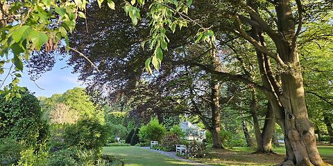 Der schöne Frühlings- und Heidegarten lädt mit weißen Bänken unter großen, schattenspendenden Bäumen zur Erholung und Entspannung ein.