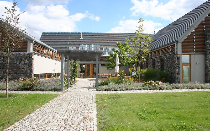 Ansicht vom Innenhof auf den Hornoer Krug, mittig im Hintergrund ist das Gebäude, in welches der Haupteingang führt. Links und rechts steht jeweils ein Seitengebäude. Ein Weg führt mittig zum Hauptgebäude. In der Mitte befindet sich ein Querweg, an dessen Rand Grünpflanzen gepflanzt wurden.