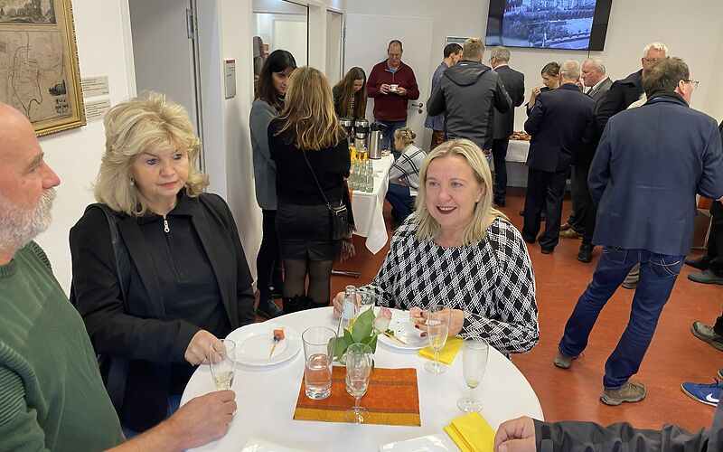 Simone Taubenek und Dagmar Klinke an einem runden Tisch im Lesesaal des Archivs. Im Hintergrund stehen weitere Besucher.