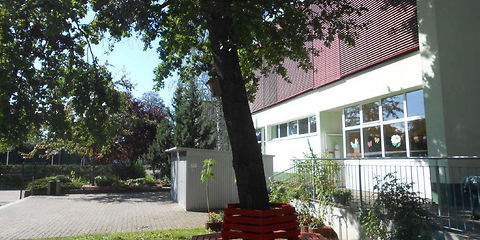 Außenbereich das Hortgebäudes mit einer roten Bank die um einen Baum herum gebaut wurde