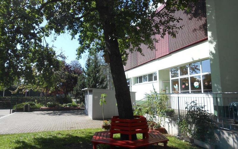 Außenbereich das Hortgebäudes mit einer roten Bank die um einen Baum herum gebaut wurde