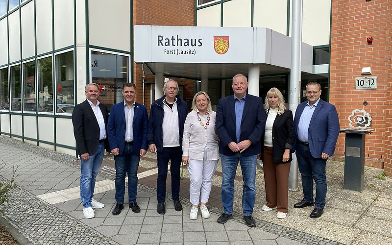 Gruppenfoto vor dem Besuchereingang des Rathauses in der Lindenstraße, im Hintergrund die Grenzrose.