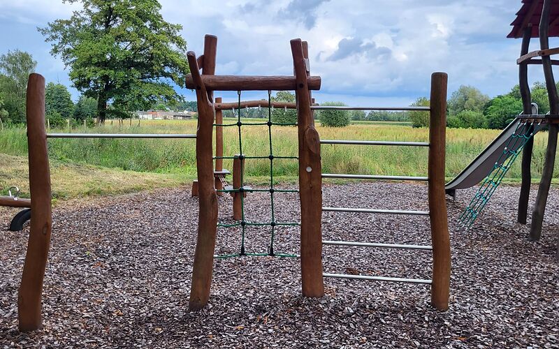 Ein Spielgerät mit drei Bereichen, die durch Holzstangen abgegrenzt sind. Feld 1: einzelne Kletterstange, Feld 2: Kletternetz, Feld 3: mehrere Stangen übereinander.