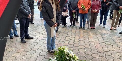 Eine Schülerin steht vor den Stolpersteinen während der Gedenkveranstaltung. Um die Steine herum liegen Blumen.