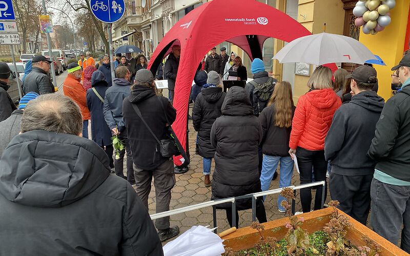 Die Teilnehmer stehen um den roten Pavillien versammelt, unter dem die Bürgermeisterin eine Rede hält.