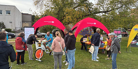 Mehrere Personen am Stand der Stadtverwaltung Forst, der aus zwei offenen Pavillionen besteht. Eine Person sitzt auf dem Smoothie-Bike (Fahrrad, auf dem vorn ein Mixer angebaut ist).