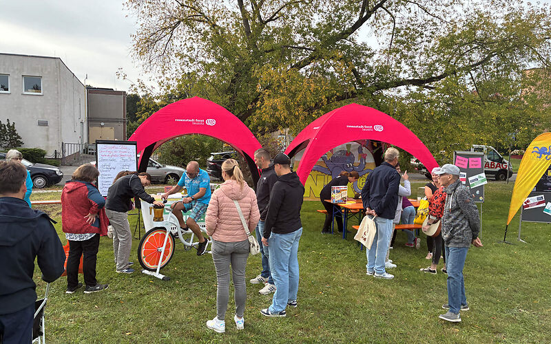 Mehrere Personen am Stand der Stadtverwaltung Forst, der aus zwei offenen Pavillionen besteht. Eine Person sitzt auf dem Smoothie-Bike (Fahrrad, auf dem vorn ein Mixer angebaut ist).