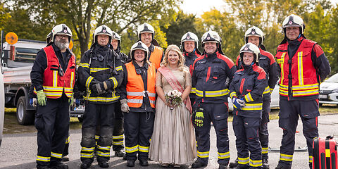 Die Forster Rosenkönigin steht inmitten einer Gruppe Feuerwehrleute, die eine Uniform tragen.