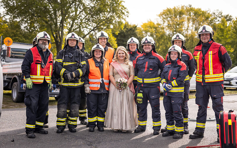 Die Forster Rosenkönigin steht inmitten einer Gruppe Feuerwehrleute, die eine Uniform tragen.