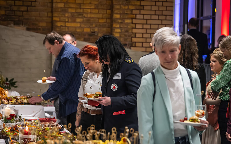 Die Gäste nehmen sich etwas vom Buffet, u.a. gibt es Burger, belegte Brötchen und Gebäck. 