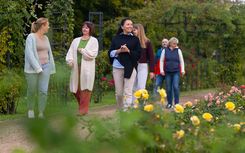 Eine Führung im Rosengarten mit sechs Personen. Im Vordergrund sind gelbe Rosen zu sehen. 