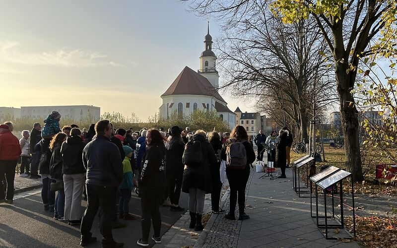 Die Teinehmenden an der Veranstaltung mit etwas Abstand von hinten fotigrafiert, im Hintergrund ist die Stadtkirche St. Nikolai zu sehen.