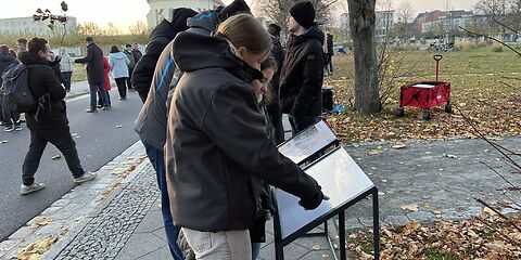 Schülerinnen und Schüler schau auf Informationstafeln, auf der Straße und auf dem Gehweg stehen weitere Teilnehmende an der Veranstaltung.