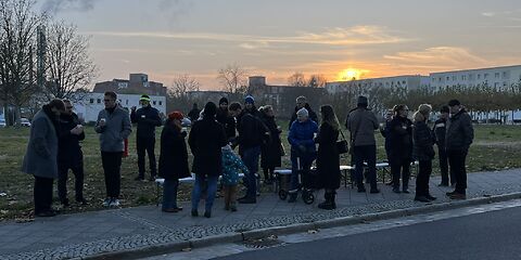 Nach der Veranstaltung reden die Teilnehmenden miteinander, inzwischen tritt die Dämmerung ein. Am klaren Himmel ist die Fluglinie eines Flugzeugs zu sehen.