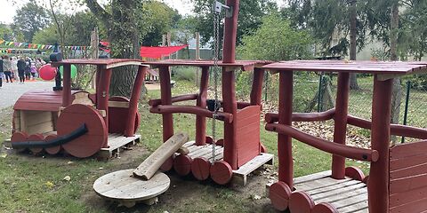 Ein Zug aus holz mit einer Lockomotive und 2 Waggons auf der Wiese des Freigeländes der Kita Kinderland. 