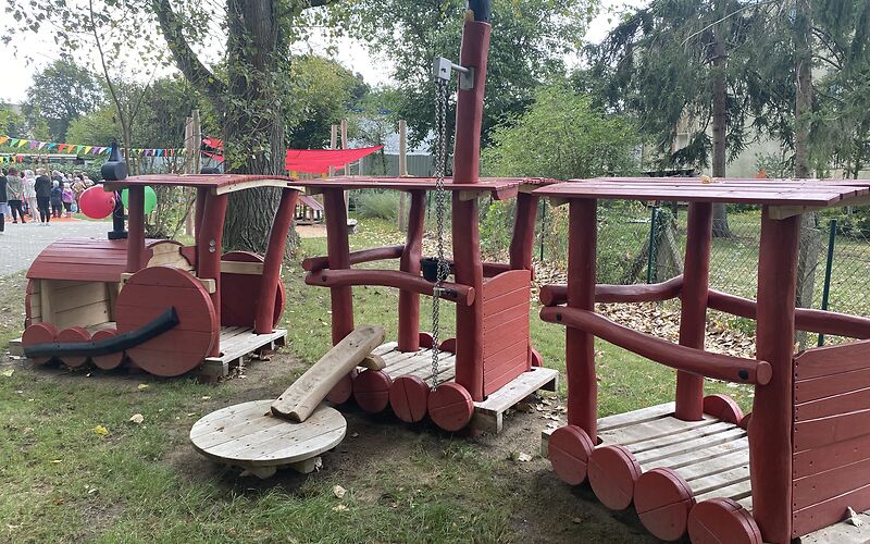 Ein Zug aus holz mit einer Lockomotive und 2 Waggons auf der Wiese des Freigeländes der Kita Kinderland. 