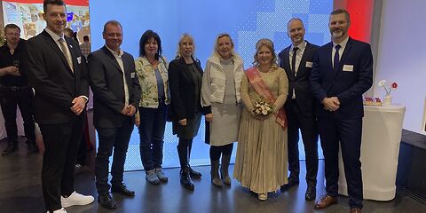 Die Bürgermeisterin und die Rosenkönigin stehen mit mehreren der Teilnehmenden vor ein blauen Leinwand mit der Aufschrift "Forster. Museum für Textil- und Industriegeschichte".