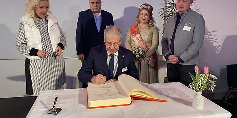 Harald Altekrüger trägt sich an einem Tisch in das Goldene Buch der Stadt Forst (Lausitz) ein. Hinter ihm stehen die Bürgermeisterin, der Vorsitzende der Stadtverordnetenversammlung und die Rosenkönigin.