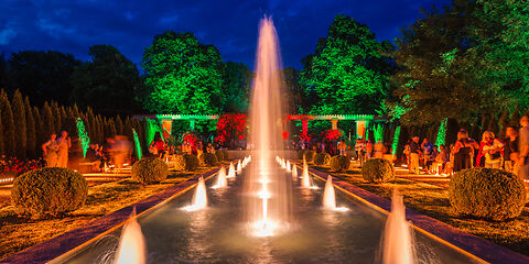 Die Großen Wasserspiele in der bunten Lichtillumination am Spätabend mit vielen Besuchern. 