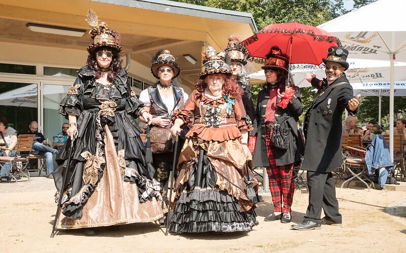 Vor dem Restaurant Rosenflair stehen 6 Personen in Steampunk-Outfits (Kleider bzw. Anzug).