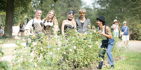 Mehrere Besucher des Festivals hinter einem Rosenbeet im Rosengarten, 5 davon zentral im Bild und weitere im Hintergrund. 