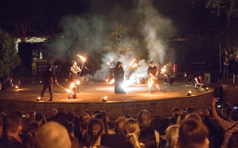 Die Feuershow auf der Wehrinselbühne, mehrere Männer mit Stangen, an deren Enden Flammen brennen. 