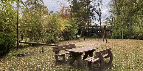 Im Vordergrund befindet sich ein Holztisch mit zwei Bänken, dahinter steht eine Holzwippe.