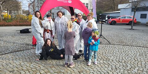 Eine Gruppe Frauen in weißen Schutzanzügen, eine Frau in schwarzer Kleidung und 3 Kinder.