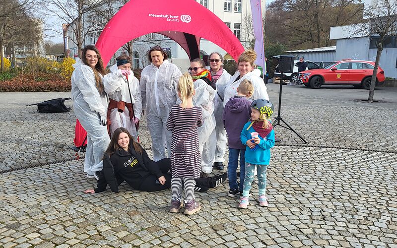 Eine Gruppe Frauen in weißen Schutzanzügen, eine Frau in schwarzer Kleidung und 3 Kinder.