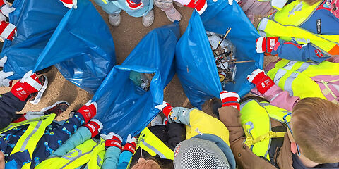 Blick von oben auf eine Gruppe Kinder, die um drei bllaue Müllsäcke stehen und diese aufhalten. 