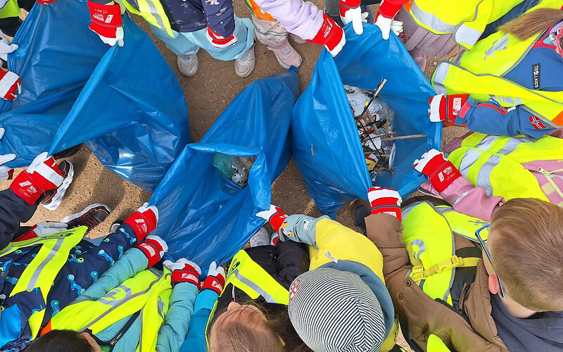 Blick von oben auf eine Gruppe Kinder, die um drei bllaue Müllsäcke stehen und diese aufhalten. 
