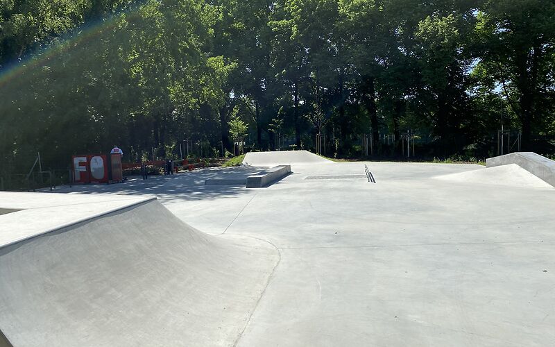 Leere Skateanlage mit Betonrampen vor einem Hintergrund aus Bäumen bei Sonnenschein