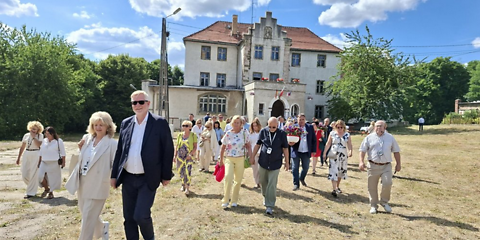 Eine große Gruppe Menschen läuft auf der ausgetrockeneten Wiese vor dem Schloss Dolzig, einem weißen Gebäude mit drei Fensterreihen.