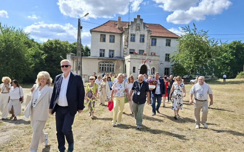Eine große Gruppe Menschen läuft auf der ausgetrockeneten Wiese vor dem Schloss Dolzig, einem weißen Gebäude mit drei Fensterreihen.