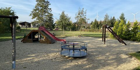 Mittig steht das Karussel, rechts ist das Klettergerüst und links die Rutsche, die an einer überdachten Holzbank befestigt ist.