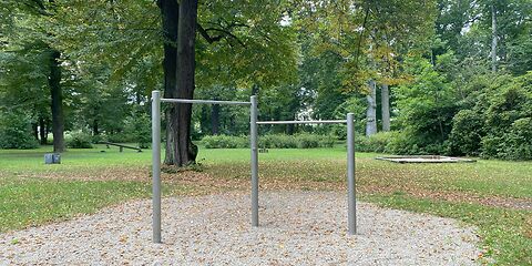 Spielgerät aus 3 Pfeilern sind oben auf 2 unterschiedlichen Höhen Metallstangen befestigt. Das Spielgerät steht auf einer Sandfläche.