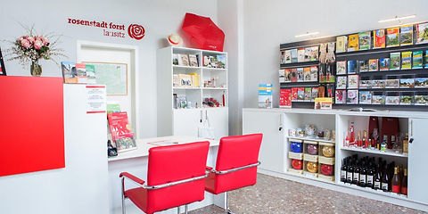Innensicht der Toursitinformation, heller freundlicher Raum, Regale mit Informationsmaterial und Andenken, Beratungstisch mit zwei roten Sesseln im Vordergrund