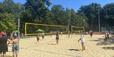 Auf einem Beachvolleyballfeld sind zwei Netze nebeneinander aufgebaut, auf denen Teams aus Kindern und Jugendlichen gegeneinander antreten.