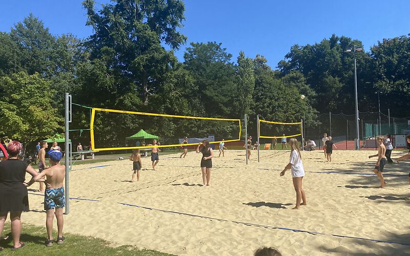 Auf einem Beachvolleyballfeld sind zwei Netze nebeneinander aufgebaut, auf denen Teams aus Kindern und Jugendlichen gegeneinander antreten.