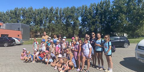 Eine Gruppe Kinder und Jugendliche platziert sich auf einem Parkplatz für ein Gruppenfoto. Die erste Reihe hockt, dahinter stehen die anderen zweireihig.