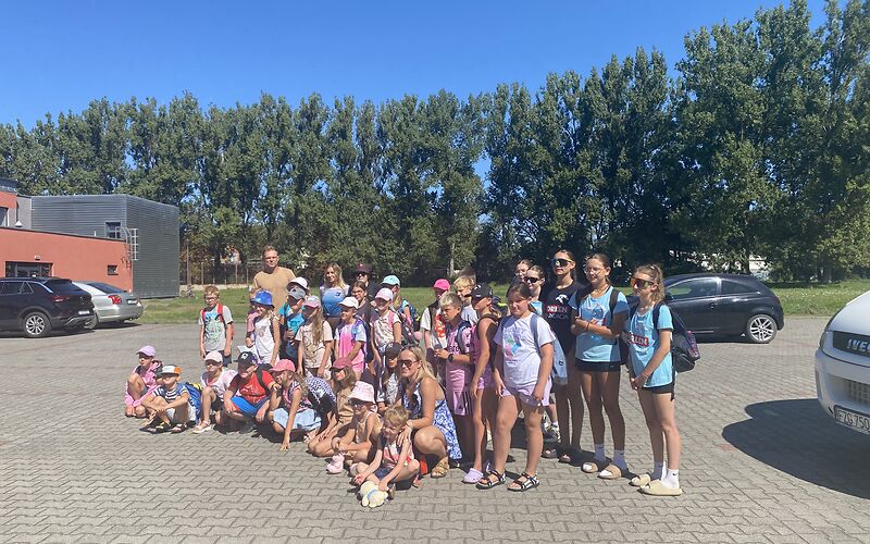 Eine Gruppe Kinder und Jugendliche platziert sich auf einem Parkplatz für ein Gruppenfoto. Die erste Reihe hockt, dahinter stehen die anderen zweireihig.