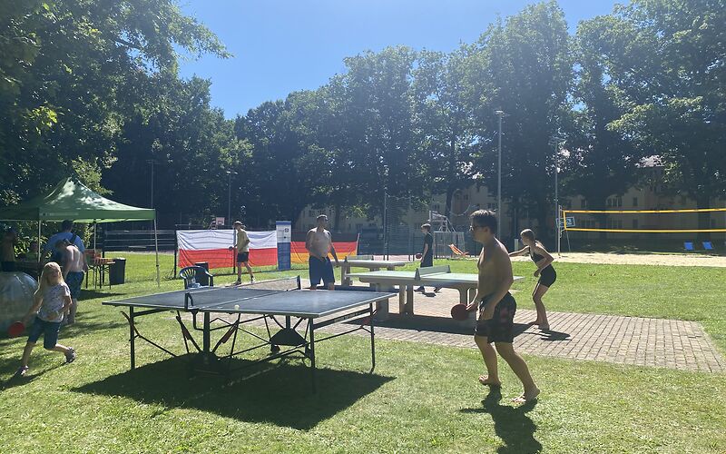 Es stehen 3 Tischtennisplatten nebeneinander, an denen jeweils zwei Personen gegeneinander spielen.