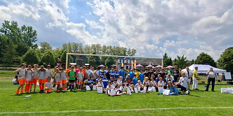 Gruppenbild vor dem Fußballtor, die Spieler, die vorn sitzen haben weiße Tüten vor sich stehen, zwei von ihnen haben einen Pokal..
